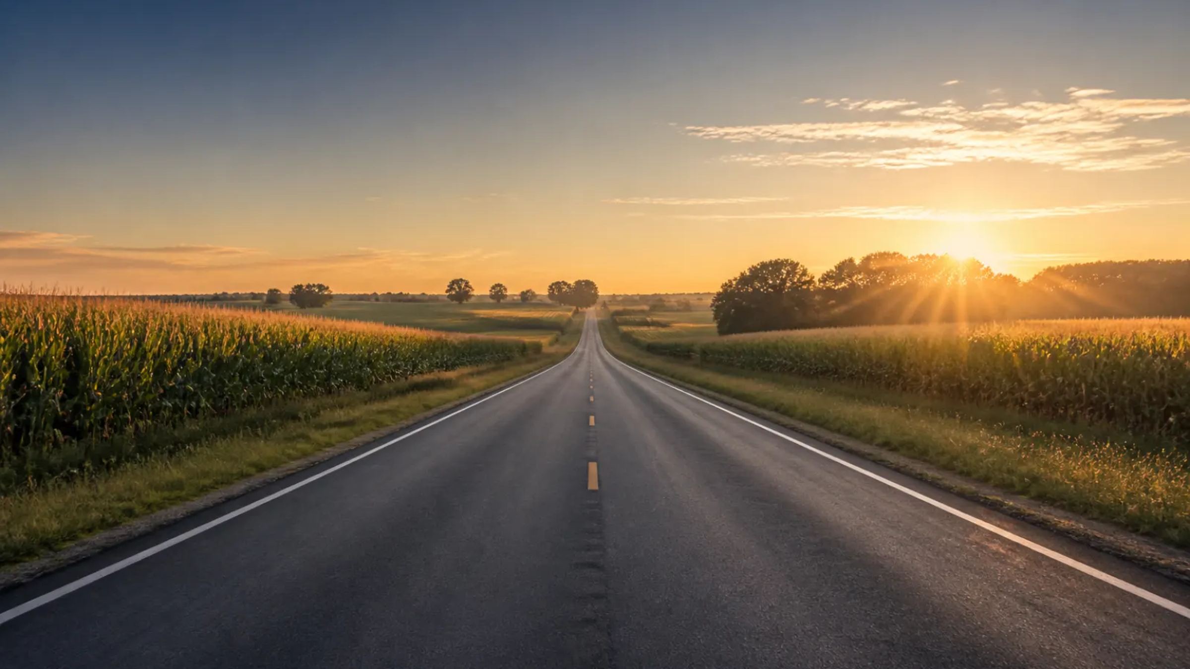 A straight two-lane highway between cornfields at sunrise